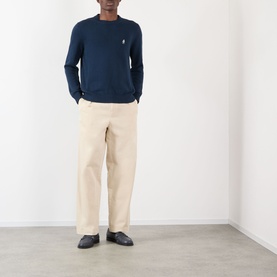 Model wearing Prada Logo Knit Sweater in navy, crew neck with embroidered logo, styled with cream wide-leg trousers and dark loafers.