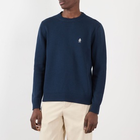 Model wearing Prada Logo Knit Sweater in navy, crew neck with embroidered logo, styled with cream trousers.