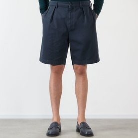 Model wearing Prada Classic Gabardine Shorts in blue, pleated cotton with belt loops, styled with navy loafers and dark green top.