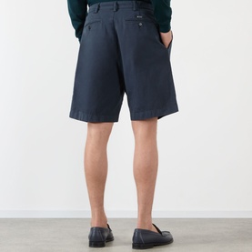 Model wearing Prada Classic Gabardine Shorts in blue, rear view showing jet pockets and logo label, styled with dark loafers.