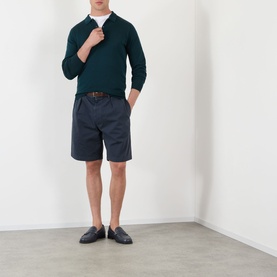 Model wearing Prada Classic Gabardine Shorts in blue with pleated detail, styled with a dark green half-zip knit and navy loafers.