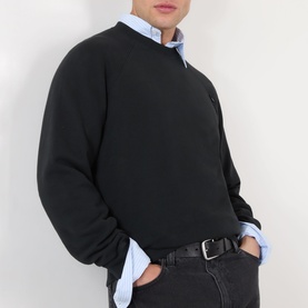 Model wearing Prada Logo Raglan Sweatshirt in black with round neck and raglan sleeves, styled over a light blue shirt with dark jeans.