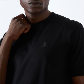 Model wearing Prada black cotton T-shirt, close-up showing tonal logo badge at chest on crew neckline.