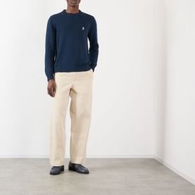 Model wearing Prada sand cotton trousers styled with a navy crew-neck sweater and black loafers.