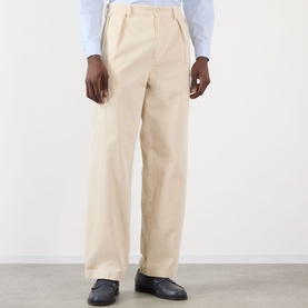 Model wearing Prada sand cotton trousers with pleated front and wide leg, styled with black loafers and light blue shirt.