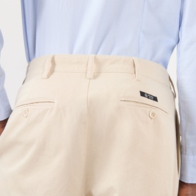 Model wearing Prada sand cotton trousers, close-up of rear view showing back pockets and logo tab, styled with a light blue shirt.