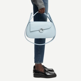 Model carrying Samsoe & Samsoe Bel Air Blue leather shoulder bag with silver ring hardware and top handle, styled with jeans and black loafers.