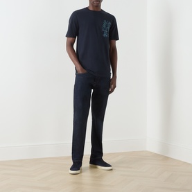 Model wearing Scotch & Soda navy cotton T-shirt with chest graphic print, styled with dark jeans and navy slip-on shoes.