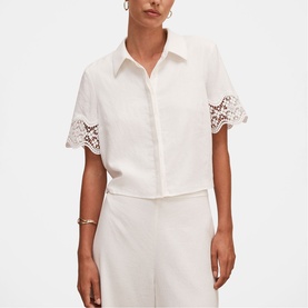 Model wearing white short-sleeve button-up shirt with floral lace cuff trim, styled with matching white wide-leg trousers