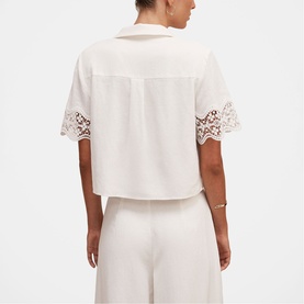 Model wearing white cropped short-sleeve shirt with lace trim detail on sleeves, styled with wide-leg white trousers, rear view.
