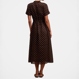 Model wearing black polka dot short sleeve midi dress with button front and cinched waist, styled with brown sandals, rear view