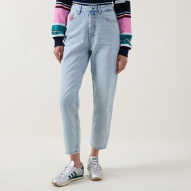 Model wearing Tommy Flag Logo Cropped Mom Jeans in Denim Light, styled with a striped knit top and green Adidas trainers.