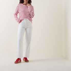 Model wearing Tommy High-Rise Slim Leg Jeans in Denim White, slim-leg fit with five-pocket style, styled with red stripe top and red trainers.