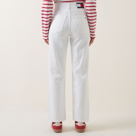 Model wearing Tommy High-Rise Slim Jeans in Denim White, back view, paired with red striped top and red shoes.
