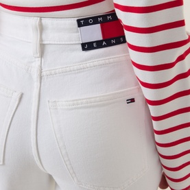 Model wearing Tommy High-Rise Slim Leg Jeans in Denim White 01, close-up of waistband with flag logo, styled with red striped top.