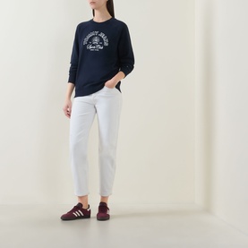 Model wearing Tommy Dark Night Navy cotton sweatshirt with chest graphic, styled with white cropped jeans and burgundy trainers.
