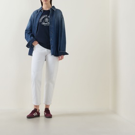 Model wearing Tommy Dark Night Navy cotton sweatshirt with denim overshirt, white cropped jeans and burgundy trainers.