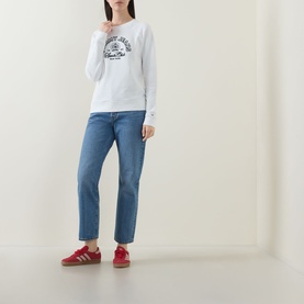 Model wearing Tommy Heritage Logo Sweatshirt in Ecru with crew neck and contrast logo graphic, styled with blue straight-leg jeans and red trainers
