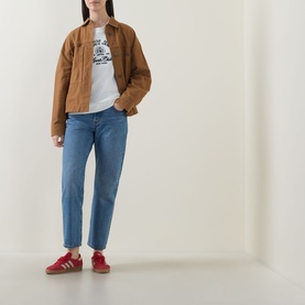 Model wearing Tommy Heritage Logo Sweatshirt in Ecru with tan jacket, blue straight-leg jeans and red trainers.