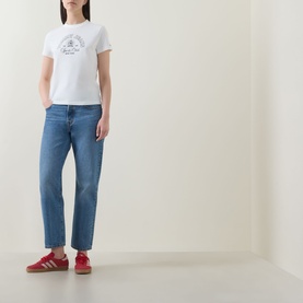 Model wearing Tommy Heritage Logo T-Shirt in Ecru with crew neck and Heritage logo graphic, styled with blue straight-leg jeans and red trainers
