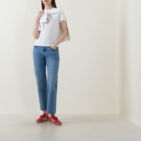Model wearing Tommy Heritage Logo T-Shirt in ecru with crew neck and front logo graphic, styled with blue straight-leg jeans and red trainers.