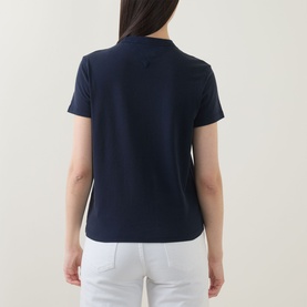 Model wearing Tommy Heritage Logo T-Shirt in Dark Night Navy, short sleeves, straight hem, shown from behind, styled with white trousers.