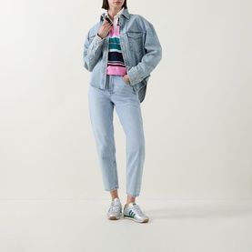 Model wearing Tommy Flag Logo Striped Rugby Top in Pink Daisy Multi Stripe, styled with light blue denim jacket, jeans and green trainers.