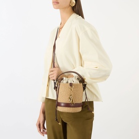 Model carrying Chloe Charm Small Basket Crossbody Bag in Crafty Brown, woven finish with leather trim and gold-tone hardware, worn crossbody