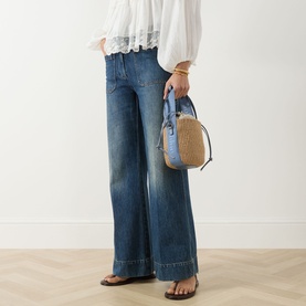 Model carrying Chloe Woody Small Basket Bag in Ashes Blue with gold-tone hardware and fixed strap, styled with wide-leg jeans and white blouse.