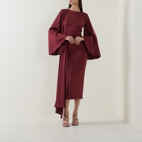 Model wearing Maisonel Draped Pencil Dress in brick, featuring wide flared sleeves, round neckline, ruched waist tie detail, midi length.