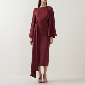 Model wearing Maisonel Draped Pencil Dress in Brick, featuring long flared sleeves, ruched waist detail and midi length, styled with strappy heels.