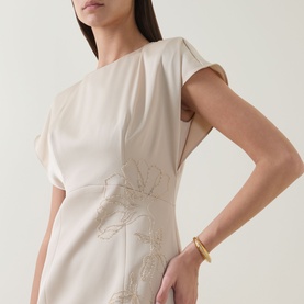 Model wearing Maisonel Floral Embellished Pencil Dress in Latte, with floral beaded embellishment detail visible. Styled with a gold cuff bracelet.