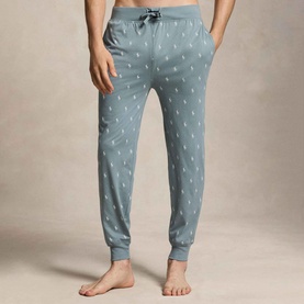 Model wearing grey jogger-style loungewear trousers with allover polo pony print and elasticated cuffs, shown cropped at waist