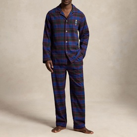 Model wearing blue and red tartan flannel pyjama set with button-front top, chest logo, and matching trousers
