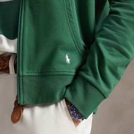 Model wearing Ralph Lauren Verano Green zip-through sweatshirt with white polo pony emblem, styled with white trousers.