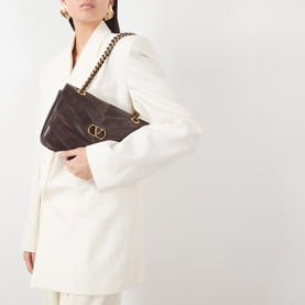Model carrying Valentino Djuna Medium Suede Shoulder Bag in Oak Brown with gold-tone V-logo hardware and braided chain strap, styled with cream