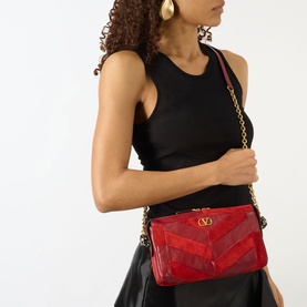 Model carrying Valentino Panthea Small Suede Shoulder Bag in Blood Red with gold-tone chain strap and V-logo detail, styled with black top and skirt