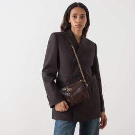 Model carrying Valentino Panthea Suede Small Shoulder Bag in Oak Brown with gold-tone chain strap and V-logo hardware, styled with dark blazer