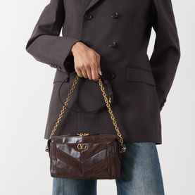 Model carrying Valentino Panthea Suede Small Shoulder Bag in Oak Brown with gold-tone chain strap and V-logo hardware, styled with grey coat and jeans