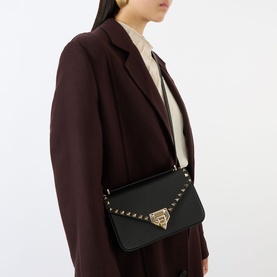 Model carrying Valentino Rockstud Small Shoulder Bag in Nero black leather, gold-tone hardware and stud trim, worn crossbody over dark blazer