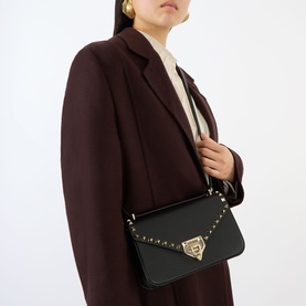 Model carrying Valentino Rockstud Small Shoulder Bag in Nero leather, gold-tone hardware and stud trim, styled with burgundy coat