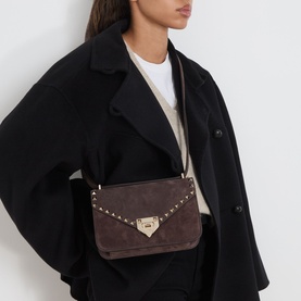 Model carrying Valentino Rockstud Small Suede Shoulder Bag in oak brown with gold-tone studs and clasp closure, styled with black coat
