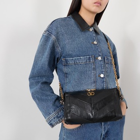 Model carrying Valentino Panthea Suede Shoulder Bag in Nero with gold-tone chain strap and chevron detail, styled with denim jacket