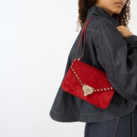 Model carrying Valentino Rockstud Small Suede Shoulder Bag in blood red with gold-tone studs and hardware, styled over denim jacket.