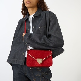 Model carrying Valentino Rockstud Small Suede Shoulder Bag in Blood Red with gold-tone hardware and stud embellishment, styled with denim jacket