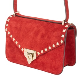 Red suede crossbody bag with gold stud trim along flap edges, gold-tone push-lock clasp, and adjustable shoulder strap