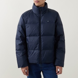 Model wearing Calvin Klein Logo Badge Padded Jacket in Dark Sapphire, stand collar, quilted design, styled with blue jeans.
