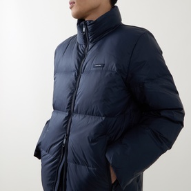 Model wearing Calvin Klein Logo Badge Padded Jacket in Dark Sapphire, featuring stand collar, quilted design and two-way front zip fastening.