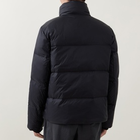 Model wearing Calvin Klein Logo Badge Padded Jacket in black, shown from behind, with stand collar, quilted design, and paired with dark trousers.
