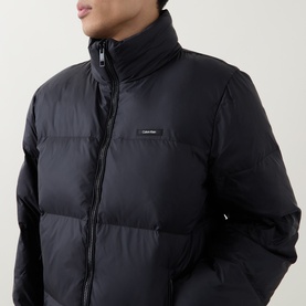 Model wearing Calvin Klein Logo Badge Padded Jacket in black, showing stand collar, two-way zip and quilted design.